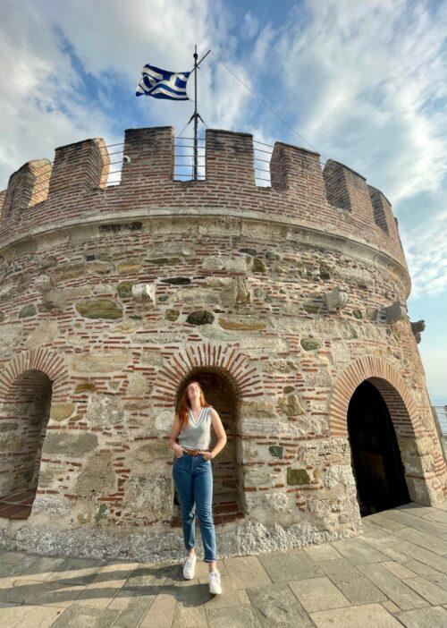 Student in front of tower with Greek flag
