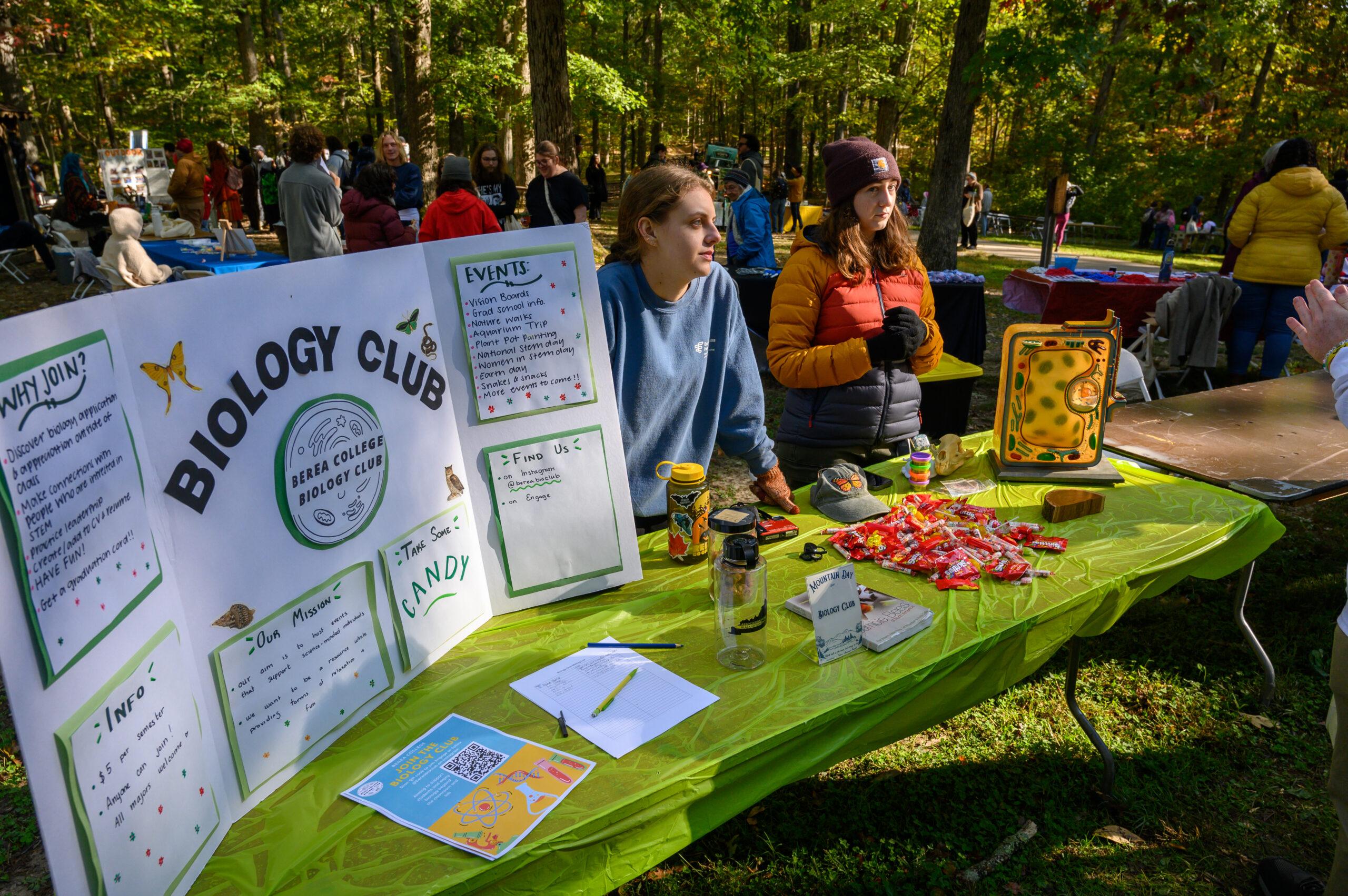 Two college students at a table outdoors, advertising the "Biology Club".
